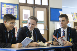 Three male students can be seen sat at a desk, reading books together.