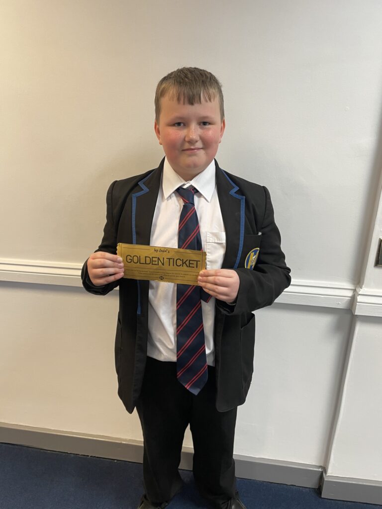 A boy smiling for a photo holding a 'golden ticket'.