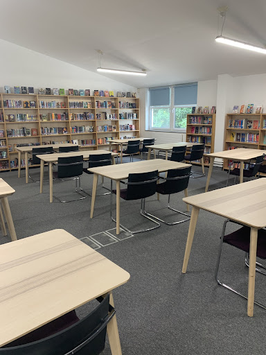 A photo of desks and chairs in the Library surrounded by bookshelves along the edges of the room.