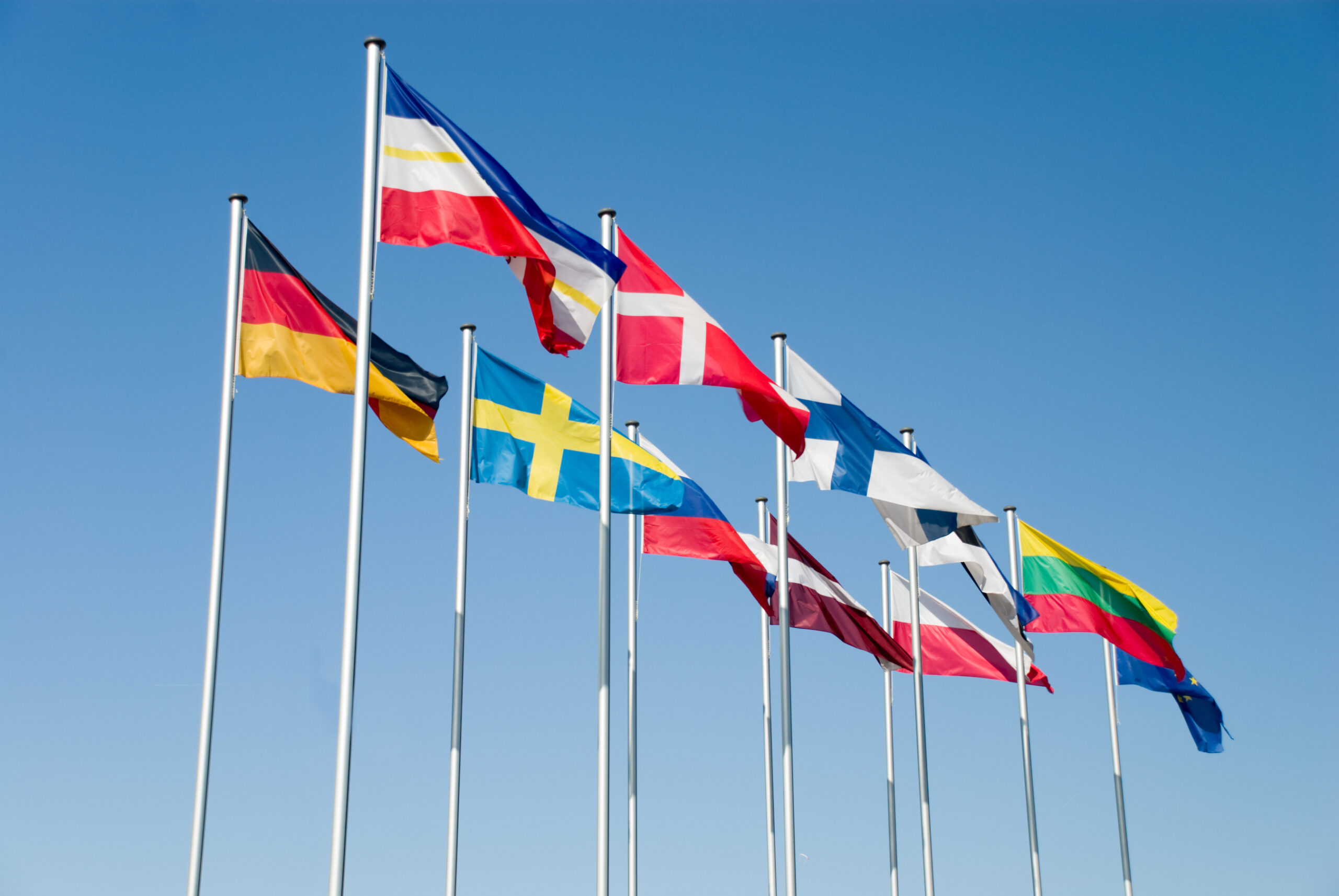 Numerous countries' flags seen flying together on poles.