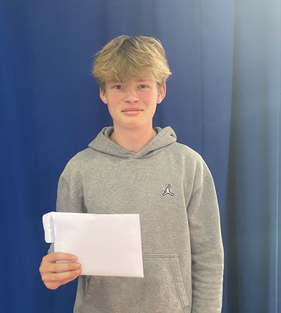 A male student seen holding his results envelope in his hands and smiling for the camera.