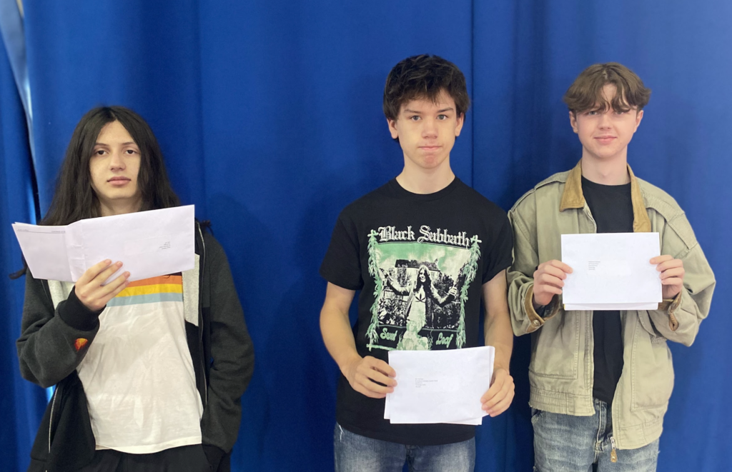Three students are pictured standing alongside one another, smiling as they open their results envelopes.