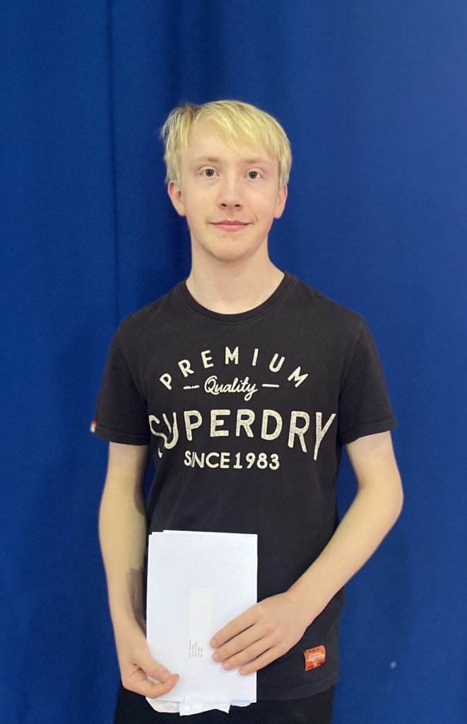 A male student seen holding his results envelope in his hands and smiling for the camera.