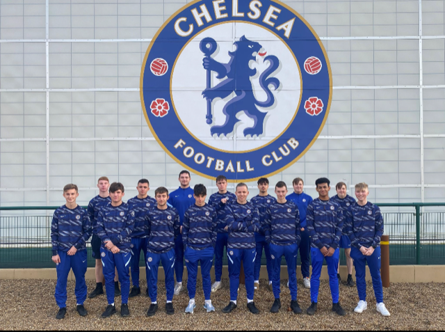 A team of footballers seen smiling for a photo in front of the Chelsea FC logo.