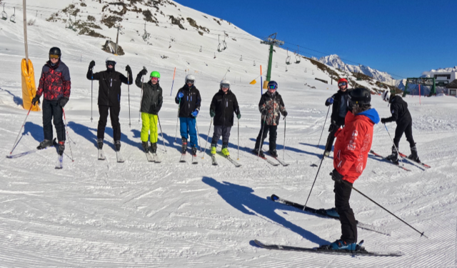 Students pictured stood in a line on a ski slope, cheering together for a group photo.