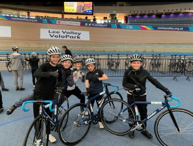 A team of cyclists pictured smiling for a photo together and stood next to their bicycles at the Velodrome in London.