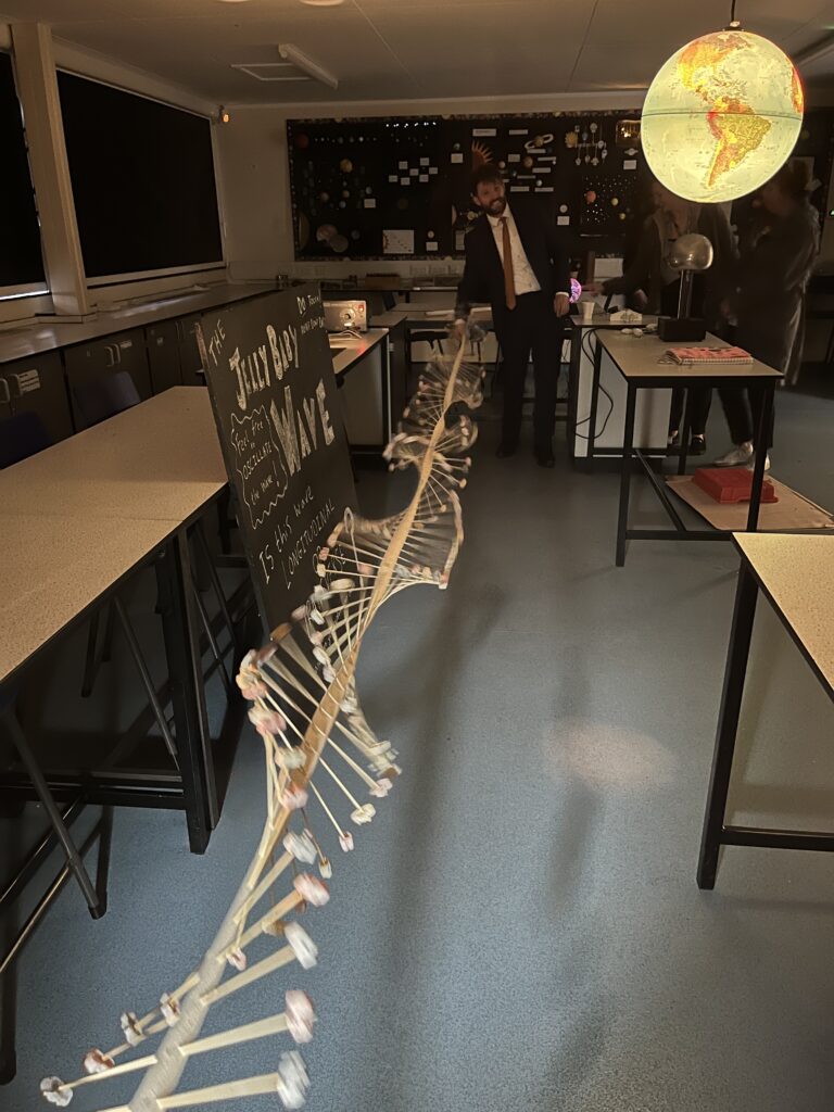 A member of staff is pictured standing alongside a large model of a DNA structure spanning the entire length of the classroom.