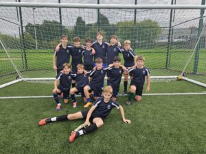 A group of boys in football kits smiling for a photo in front of a goal