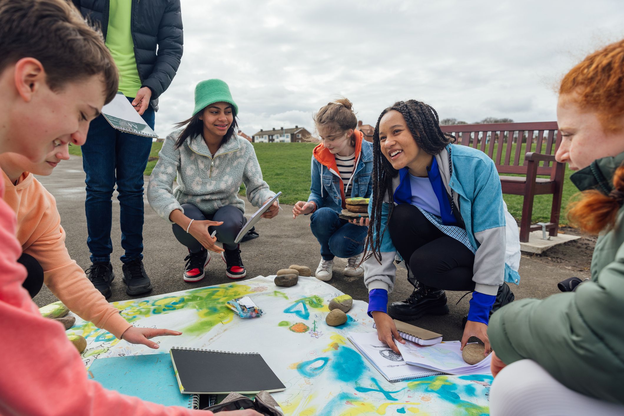 A group of teenage friends wearing casual clothing on an overcast summer day in Whitley Bay, Northeastern England. They are gathered on the promenade by the sea where they use different arts and crafts products to create sustainability artwork to spread a message of environmental conservation for Earth Day.